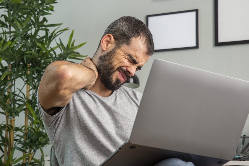 dolori al tratto cervicale curato con l'osteopatia: l'immagine di un uomo, di fronte al computer, che avverte un dolore al tratto cervicale.